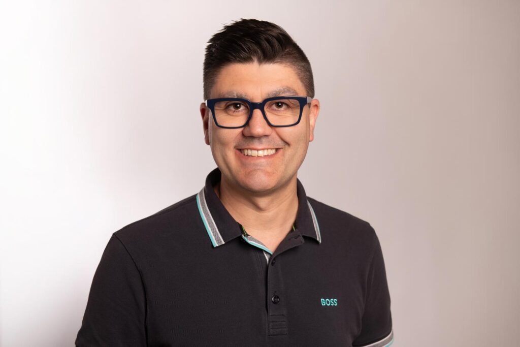 Mann mit neutralem Blick im schwarzen Poloshirt mit gruenem BOSS Logo