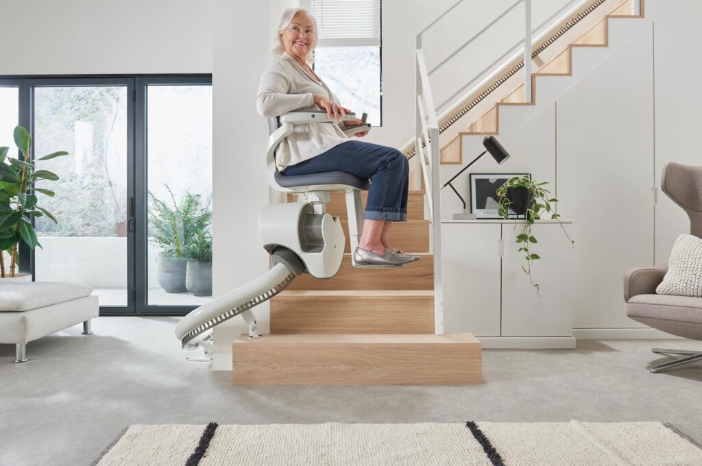 Lächelnde Frau auf weißem Treppenlift, helle Wohnung, Holzstufen