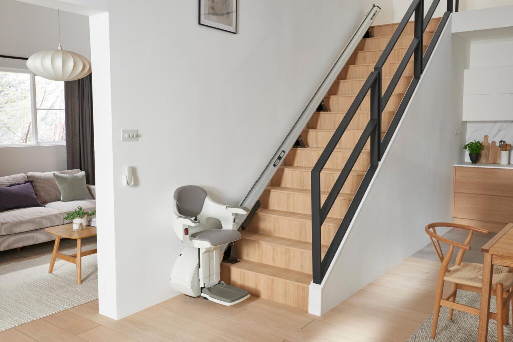 Weisser Treppenlift an Holztreppe mit schwarzem Gelaender im hellen Raum