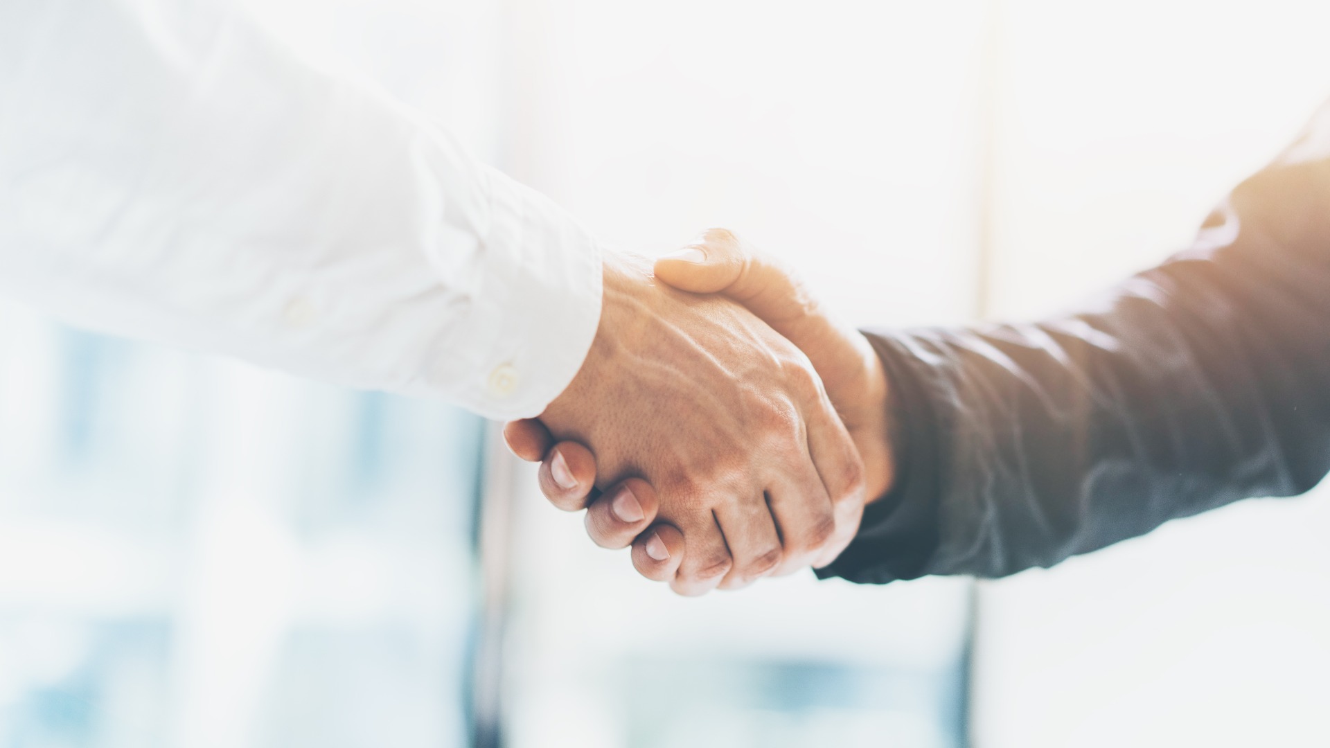 Treffen von Geschäftspartnern. Bild: Handschlag zwischen Geschäftsleuten. Erfolgreiche Geschäftsleute, die sich nach einem guten Geschäft die Hand geben. Querformat, unscharfer Hintergrund